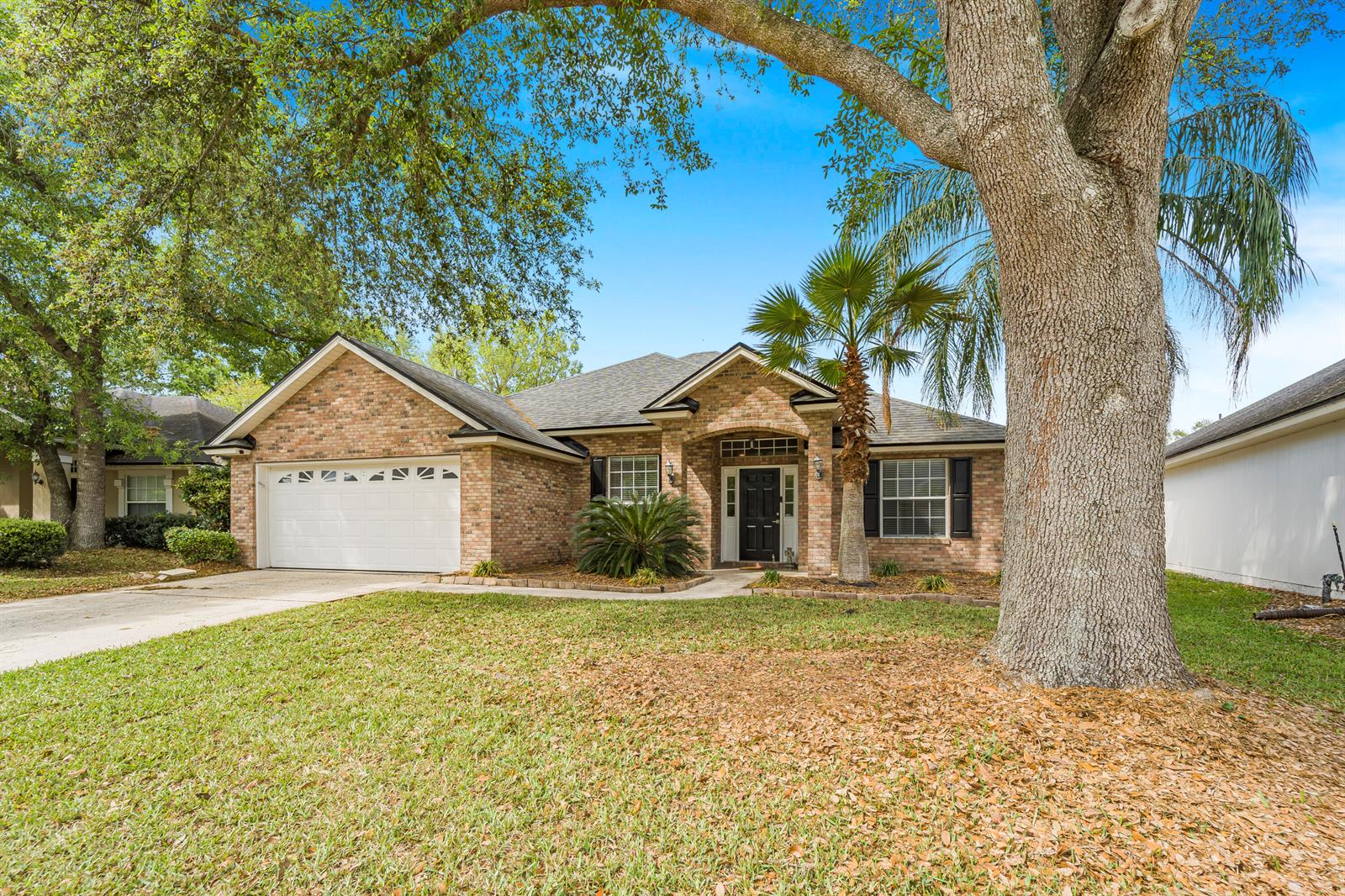 A single-story brick house with a two-car garage, a front porch, and mature trees — 908 W Doty Branch Lane, FL 32259, FL