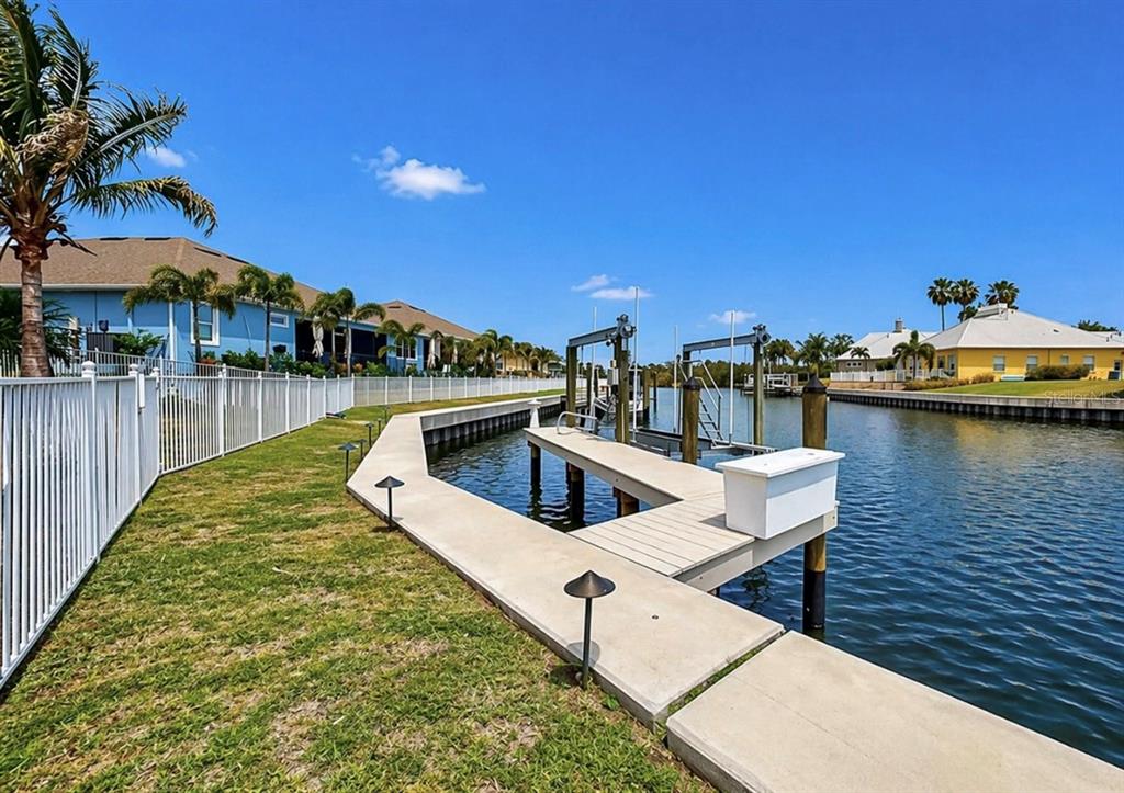 A concrete dock with a boat lift extends into a canal beside a fenced lawn — 954 SIGNET DRIVE, APOLLO BEACH, FL