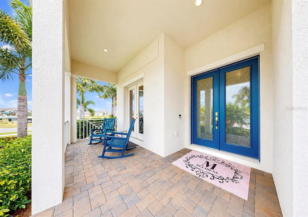 A covered porch features a paver floor, two blue rocking chairs, and blue double doors — 954 SIGNET DRIVE, APOLLO BEACH, FL
