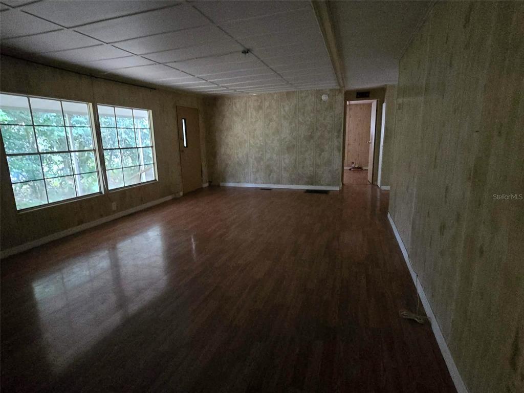 An empty living room features wood-look flooring, textured wallpaper, and a drop ceiling — 5930 SW 61ST PLACE, OCALA, FL