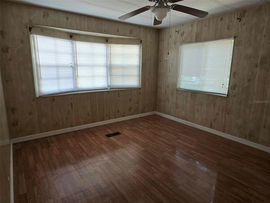 An empty room features wood-paneled walls, wood-look flooring, a ceiling fan, and multiple windows — 5930 SW 61ST PLACE, OCALA, FL