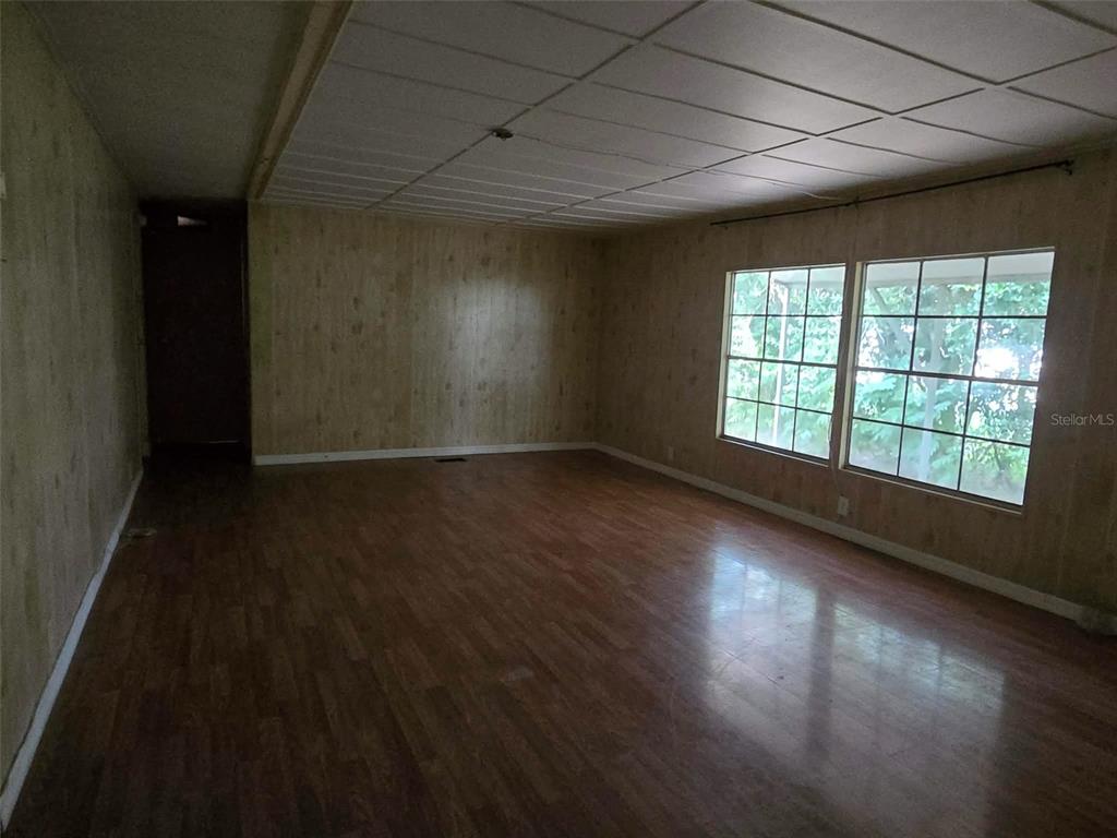 An empty room features wood-paneled walls, wood-look flooring, and a white drop ceiling — 5930 SW 61ST PLACE, OCALA, FL
