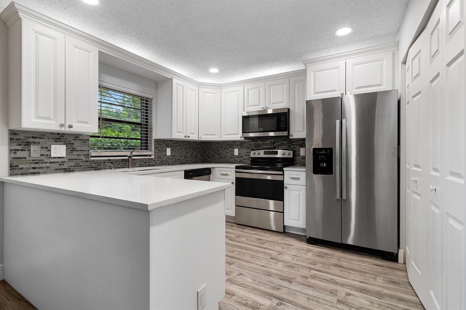 A kitchen with white cabinets, stainless steel appliances, quartz countertops, and a gray tile backsplash — 9 Vía De Casas Norte, Boynton Beach FL 33426, BOYNTON BEACH, FL