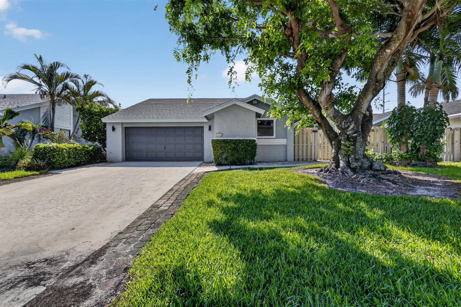 A single-story house with a gray exterior, a dark garage door, and a large tree — 1055 NW 18th Avenue, Delray Beach FL 33445, DELRAY BEACH, FL