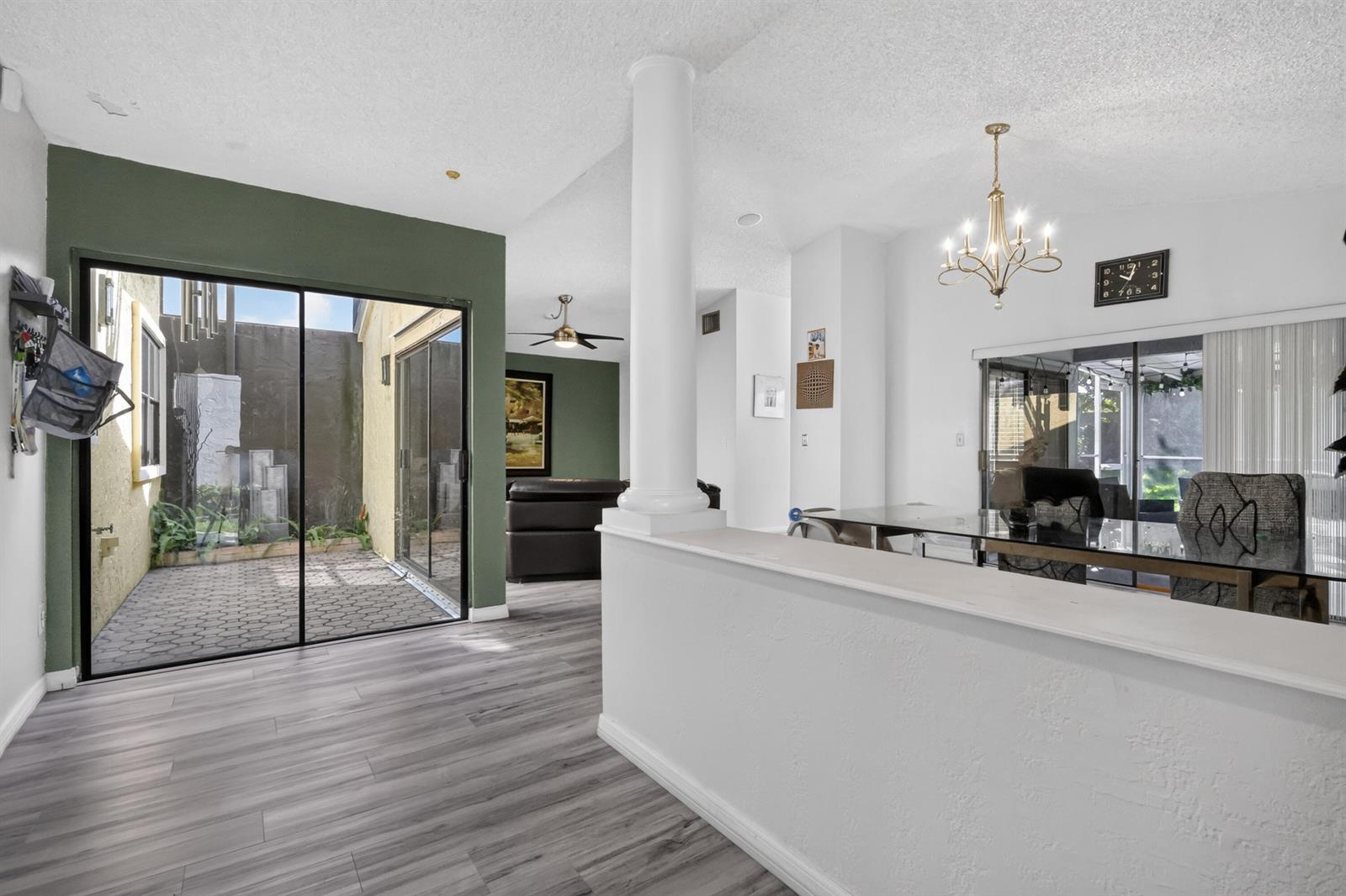 A living and dining area features wood-look flooring, a white column, and a sliding glass door — 1055 NW 18th Avenue, Delray Beach FL 33445, DELRAY BEACH, FL