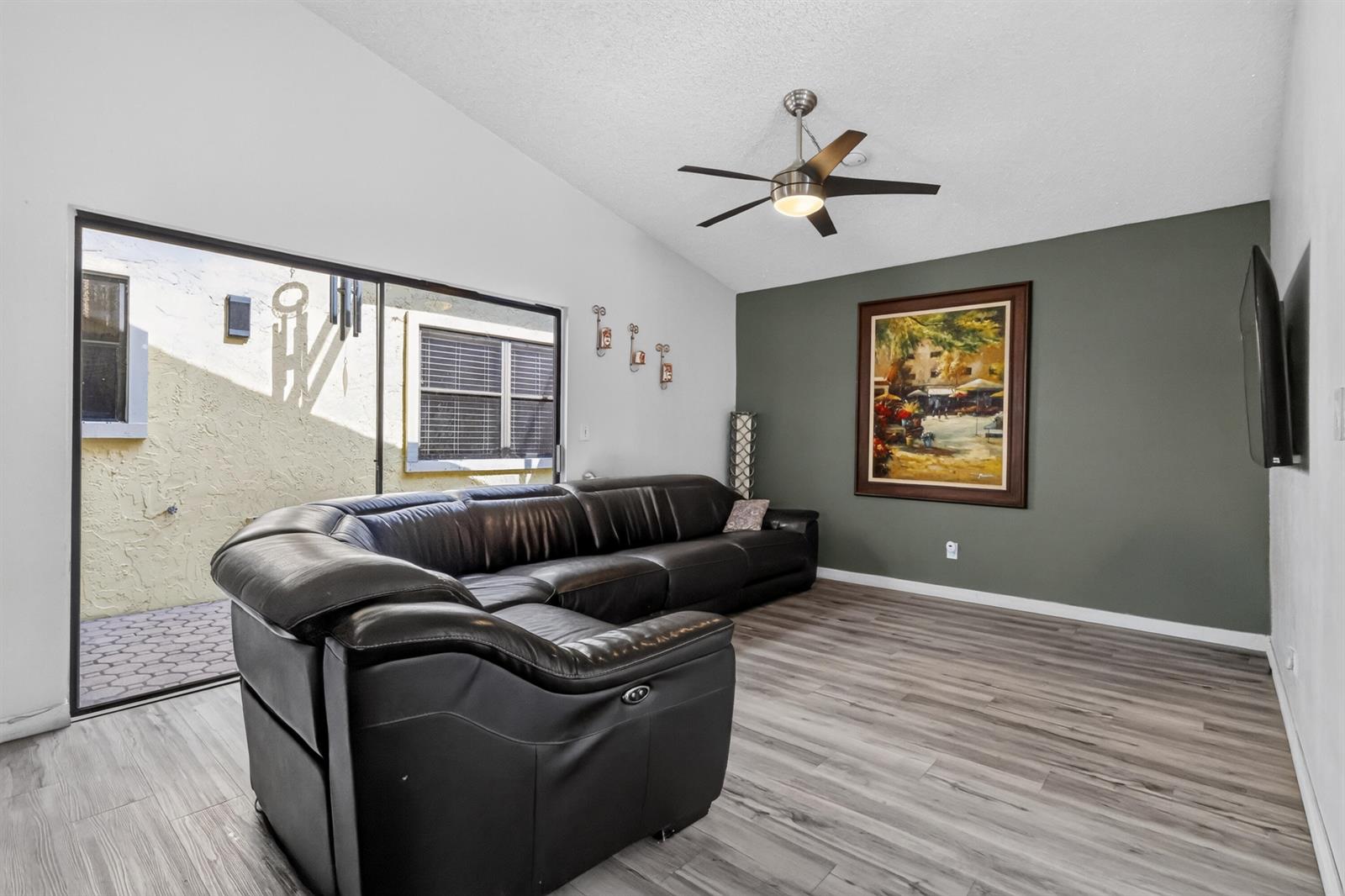 A living room features a large black sectional sofa, gray wood-look flooring, and a green accent wall — 1055 NW 18th Avenue, Delray Beach FL 33445, DELRAY BEACH, FL