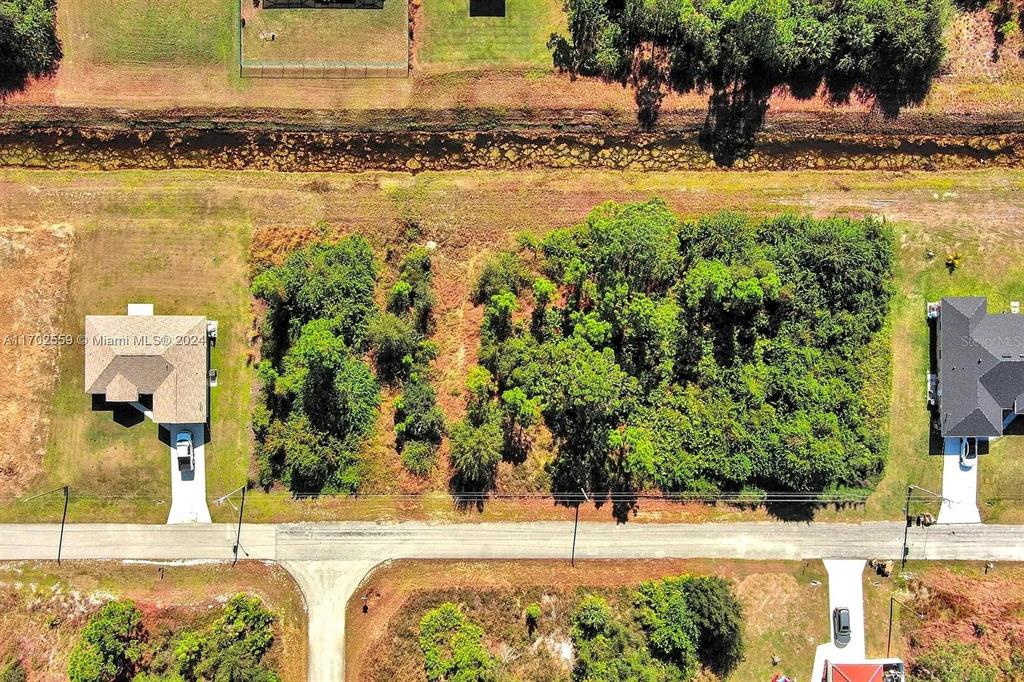 An aerial view shows a vacant, wooded residential lot situated between two existing houses — 844 CARBON STREET E, LEHIGH ACRES, FL