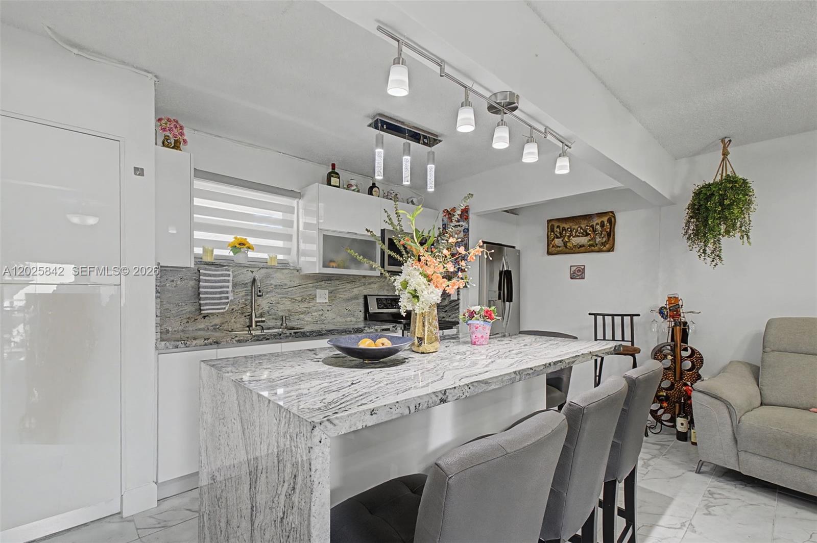 A modern kitchen features white cabinetry, granite countertops, a waterfall island, and gray bar stools — 399 NW 72nd Ave # 320, Miami FL 33126, MIAMI, FL