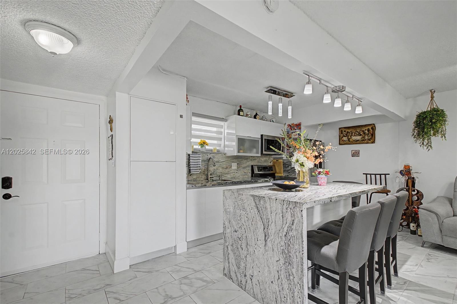 A kitchen features a white-cabinet layout, a granite waterfall island, and gray bar stools — 399 NW 72nd Ave # 320, Miami FL 33126, MIAMI, FL