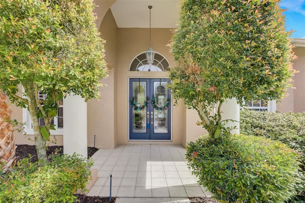 The front entrance features double blue glass-paneled doors under a covered porch with arched transom — 7650 PARTRIDGE STREET CIRCLE, BRADENTON, FL
