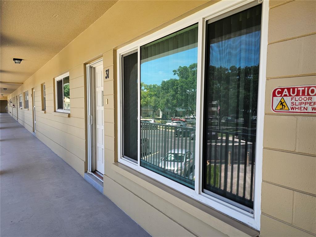A view of an exterior walkway with apartment unit doors, windows, and a caution sign — 2321 ECUADORIAN WAY UNIT 31, CLEARWATER, FL
