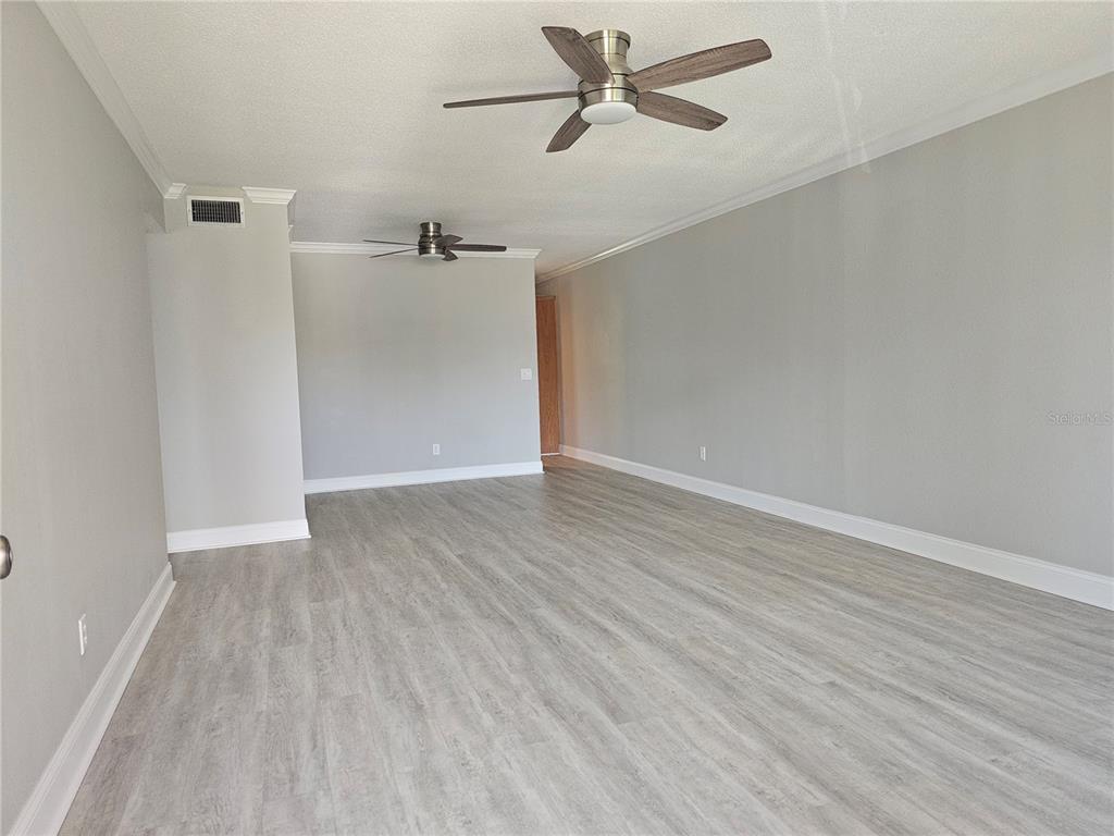 An empty room features light gray walls, wood-look flooring, and two ceiling fans — 2321 ECUADORIAN WAY UNIT 31, CLEARWATER, FL