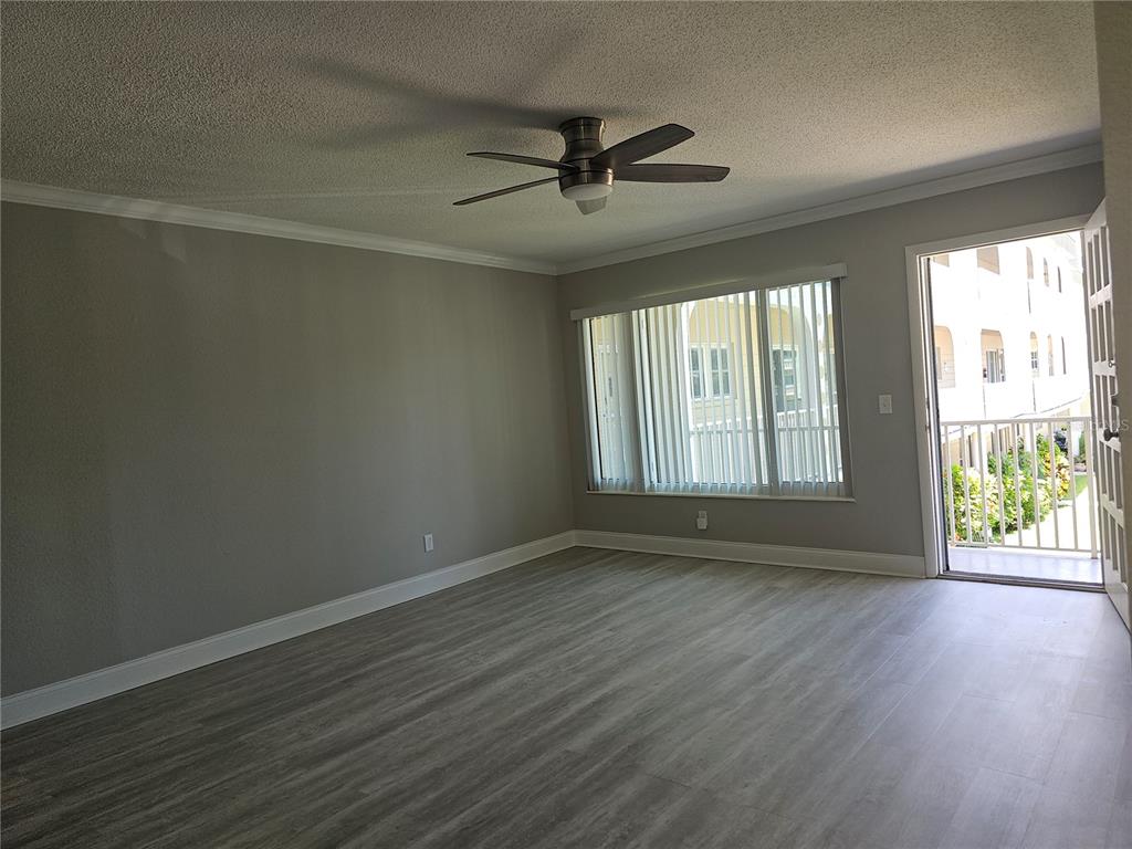 An empty room features gray walls, wood-look flooring, a ceiling fan, and a balcony door — 2321 ECUADORIAN WAY UNIT 31, CLEARWATER, FL