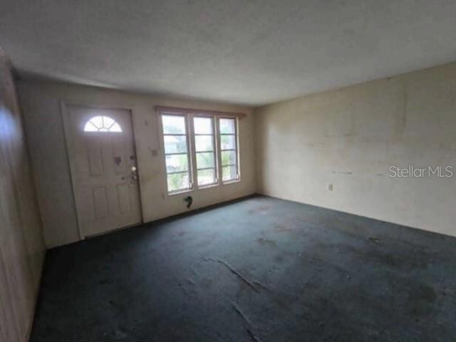 An empty room features a front door, a three-pane window, and worn gray carpeting — 13516 SANTA ROSA AVENUE, PORT CHARLOTTE, FL