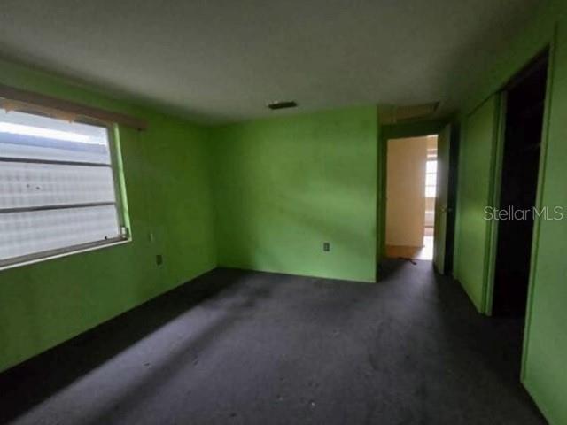 An empty room features bright green walls, dark carpeting, and a window with blinds — 13516 SANTA ROSA AVENUE, PORT CHARLOTTE, FL