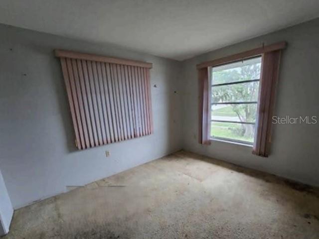 An empty bedroom features light-colored walls, a window with vertical blinds, and worn carpeting — 13516 SANTA ROSA AVENUE, PORT CHARLOTTE, FL