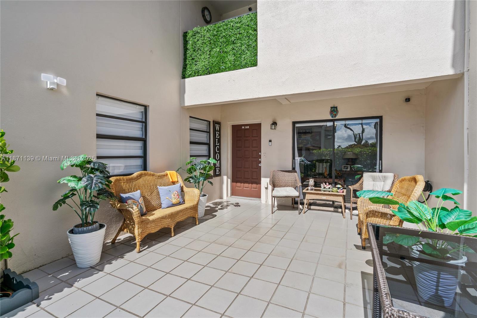 A tiled patio features wicker furniture, potted plants, and a brown front door — 13412 SW 62nd St # 103M, Miami FL 33183, MIAMI, FL