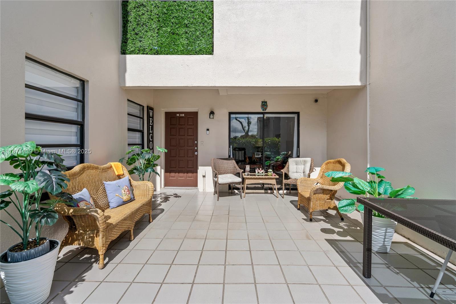 A tiled outdoor patio features wicker furniture, potted plants, and a brown entry door — 13412 SW 62nd St # 103M, Miami FL 33183, MIAMI, FL