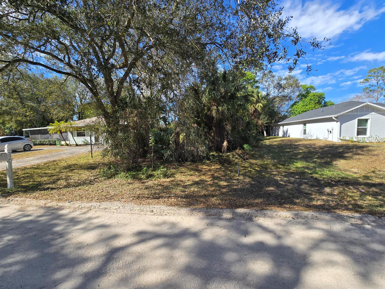 A vacant lot sits between two houses under a large tree on a sunny day — 2445 87th Court, Vero Beach FL 32966, VERO BEACH, FL