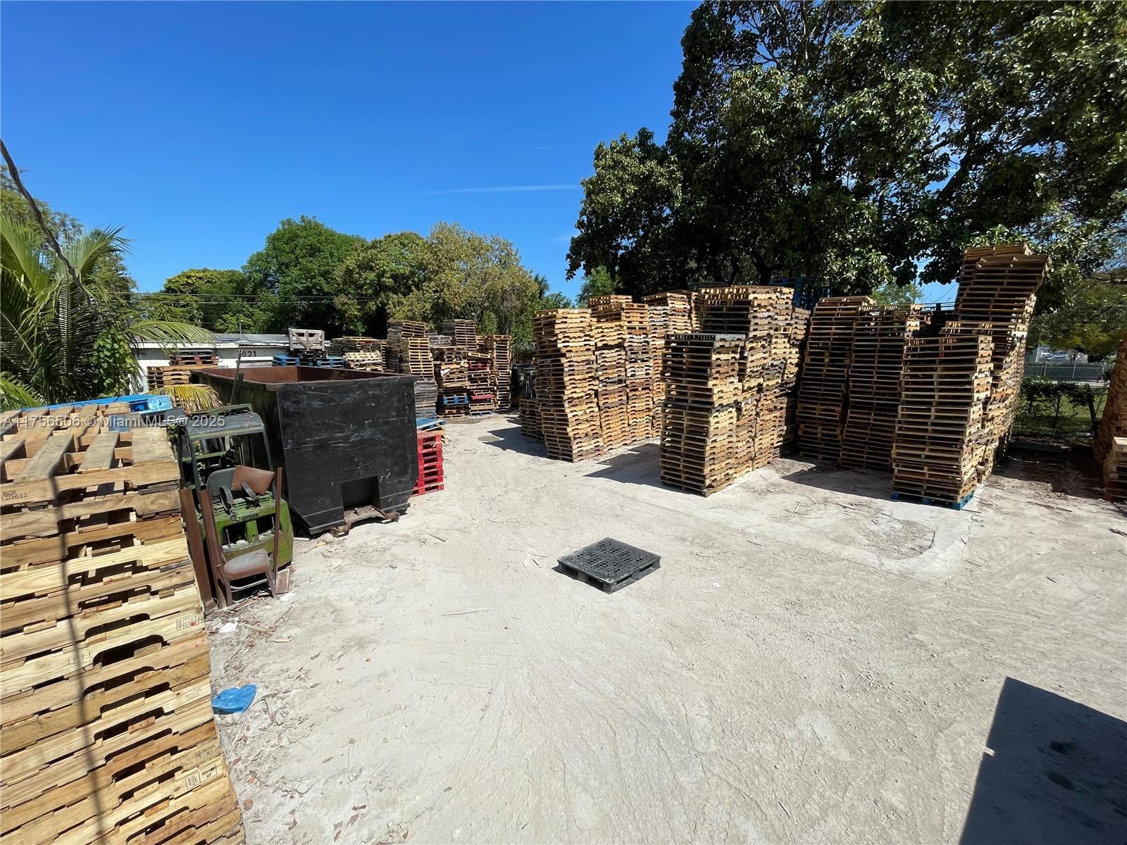 An outdoor storage yard features numerous tall stacks of wooden shipping pallets and a dumpster — 3013 NW 54th St, Miami FL 33142, MIAMI, FL