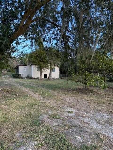 A light-colored single-story house sits on a grassy lot surrounded by large, mossy trees — 14914 SE 56TH AVENUE, SUMMERFIELD, FL