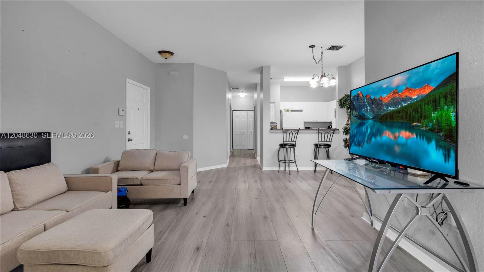 A living room features light gray wood-look flooring, neutral furniture, and an open kitchen area — 13103 SW 42nd St # 5106, Miramar FL 33027, MIRAMAR, FL