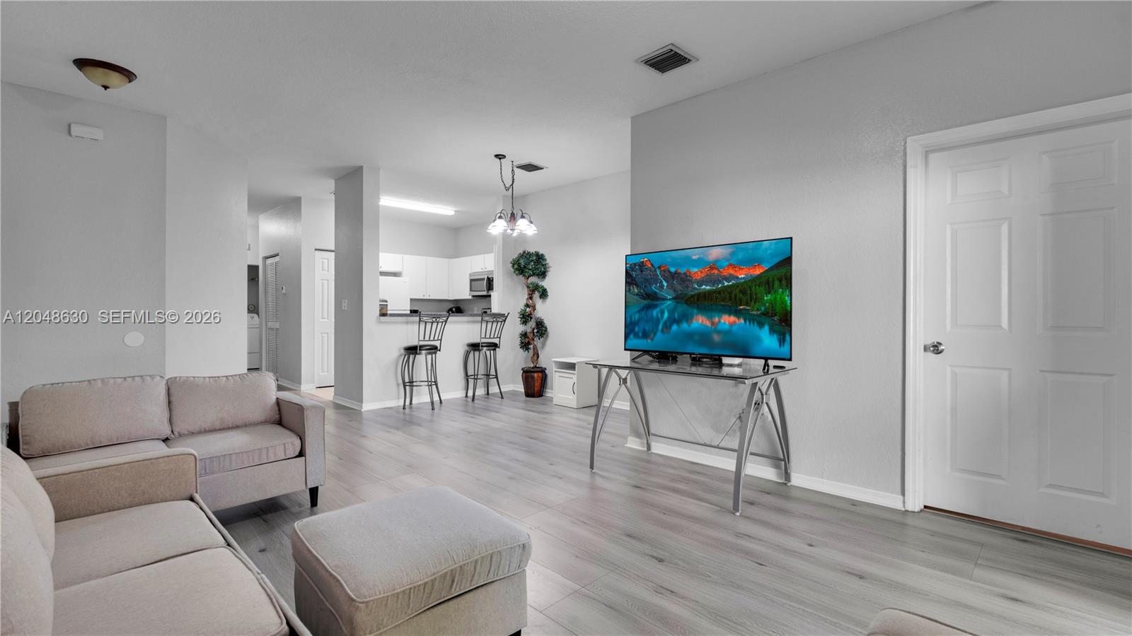 A living room features light wood-look flooring, a grey sofa, and a television on a stand — 13103 SW 42nd St # 5106, Miramar FL 33027, MIRAMAR, FL