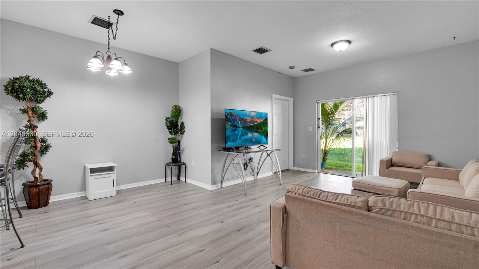 A living room features light gray walls, wood-look flooring, a television on a stand, and sliding doors — 13103 SW 42nd St # 5106, Miramar FL 33027, MIRAMAR, FL