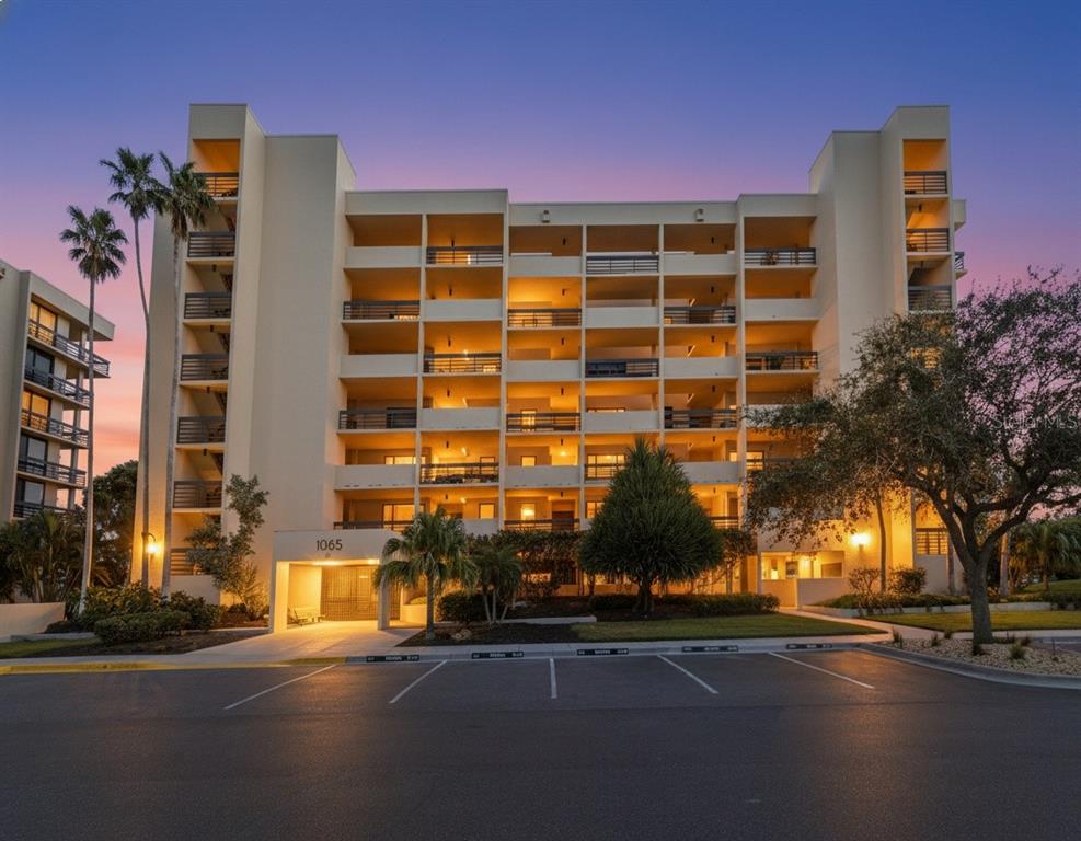A multi-story apartment building with balconies and a parking lot at sunset — 1065 GULF OF MEXICO DRIVE UNIT 305, LONGBOAT KEY, FL