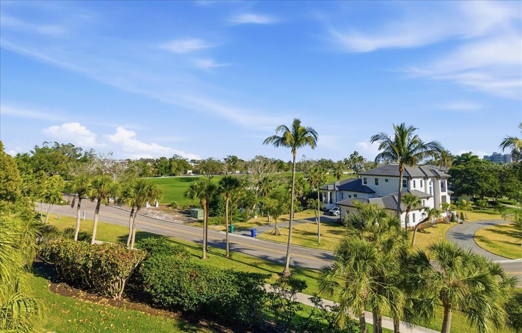 An elevated view of a suburban street with palm trees, green lawns, and a large house — 1065 GULF OF MEXICO DRIVE UNIT 305, LONGBOAT KEY, FL