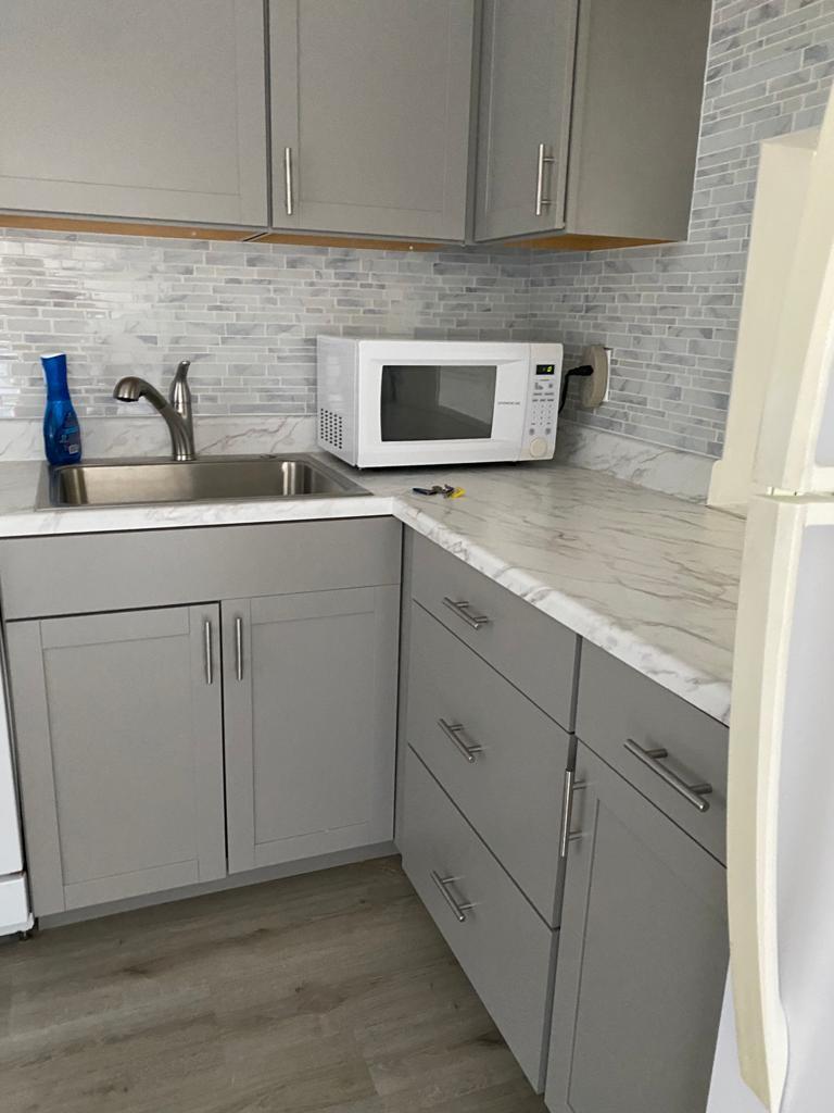 A kitchen features gray cabinets, a white microwave, a stainless steel sink, and marble-patterned countertops — 19 Abbey Lane # 206, Delray Beach FL 33446, DELRAY BEACH, FL