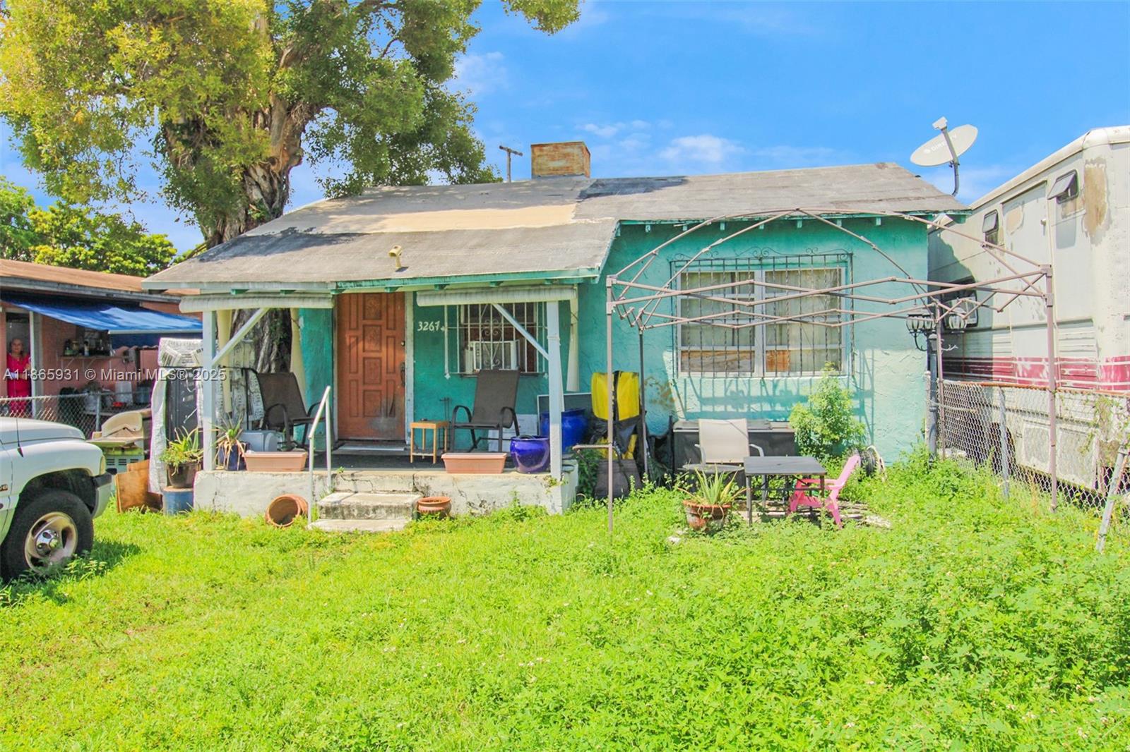A teal, single-story house with a front porch, metal roof, and overgrown yard — 3270 NW 36th St, Miami FL 33142, MIAMI, FL