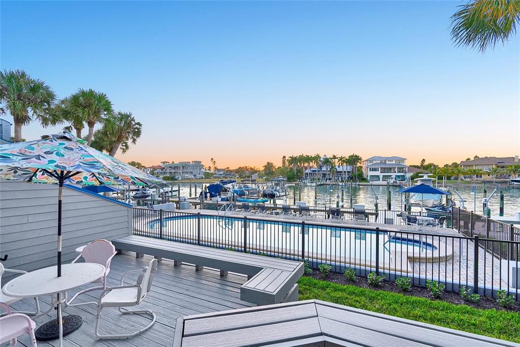 A deck with a pool, patio furniture, and a view of a boat-filled marina — 910 PINELLAS BAYWAY S UNIT 107, TIERRA VERDE, FL