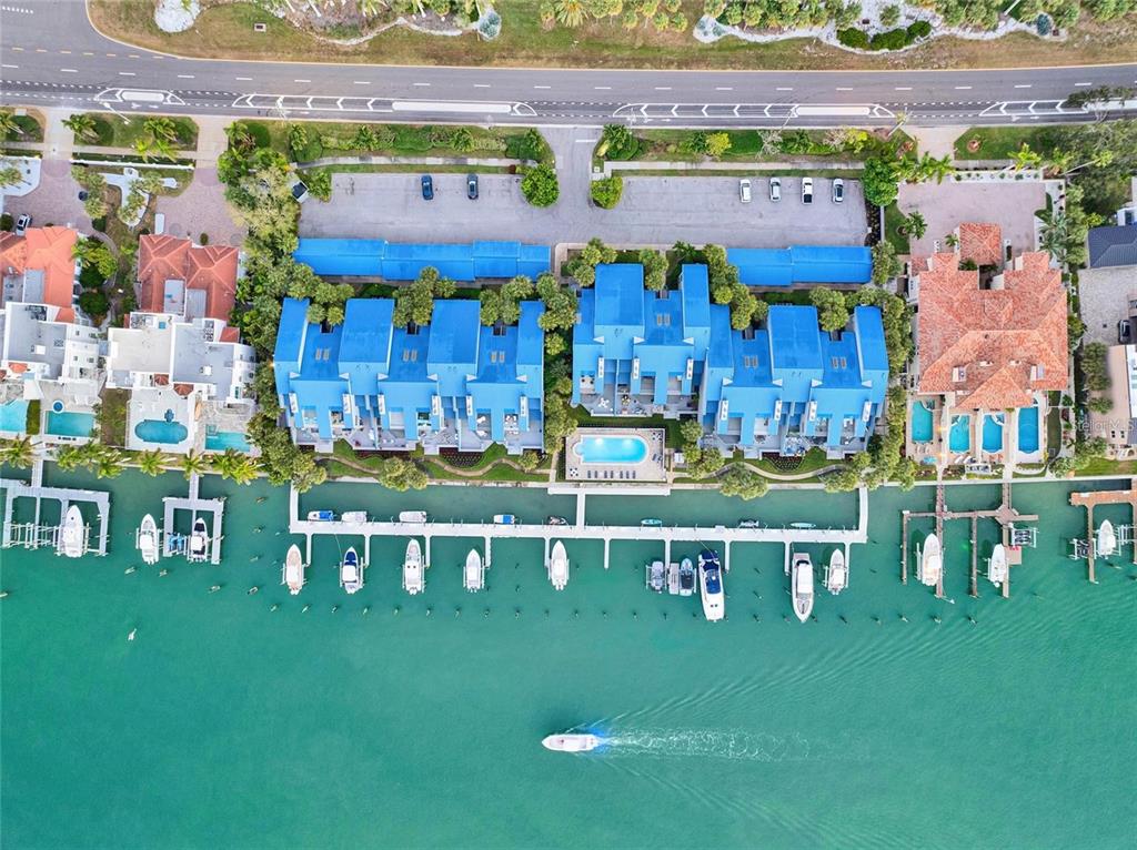 An aerial view shows a waterfront townhouse complex with a pool, boat slips, and parking — 910 PINELLAS BAYWAY S UNIT 107, TIERRA VERDE, FL