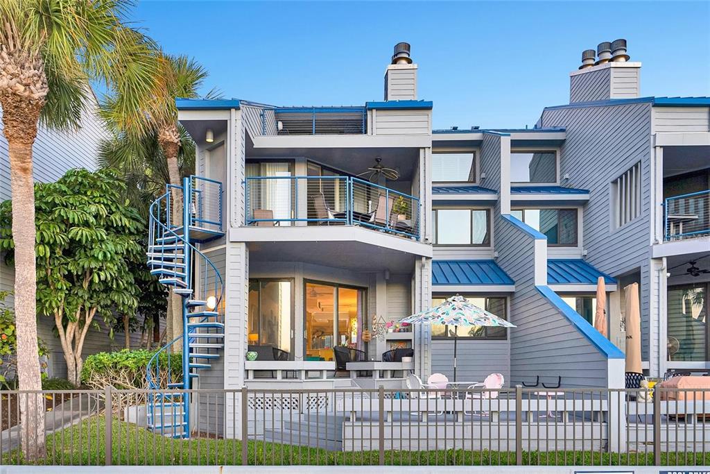 A multi-story gray townhouse features a spiral staircase, balconies, and a ground-level patio area — 910 PINELLAS BAYWAY S UNIT 107, TIERRA VERDE, FL