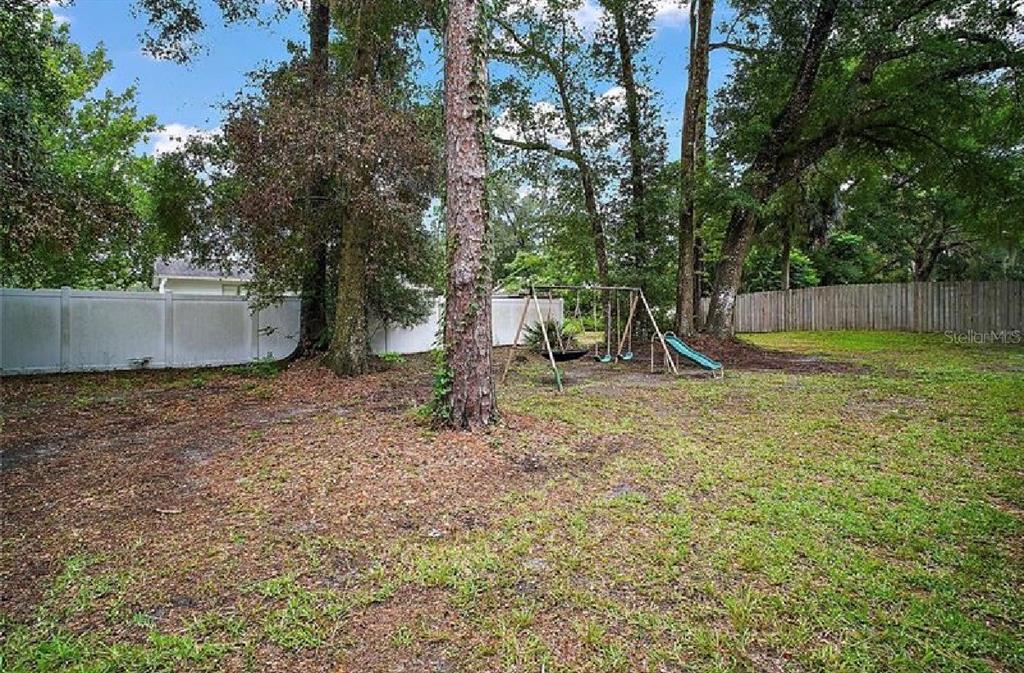 A backyard features a swing set, mature trees, and a white vinyl privacy fence — 2404 NE 32ND PLACE, OCALA, FL