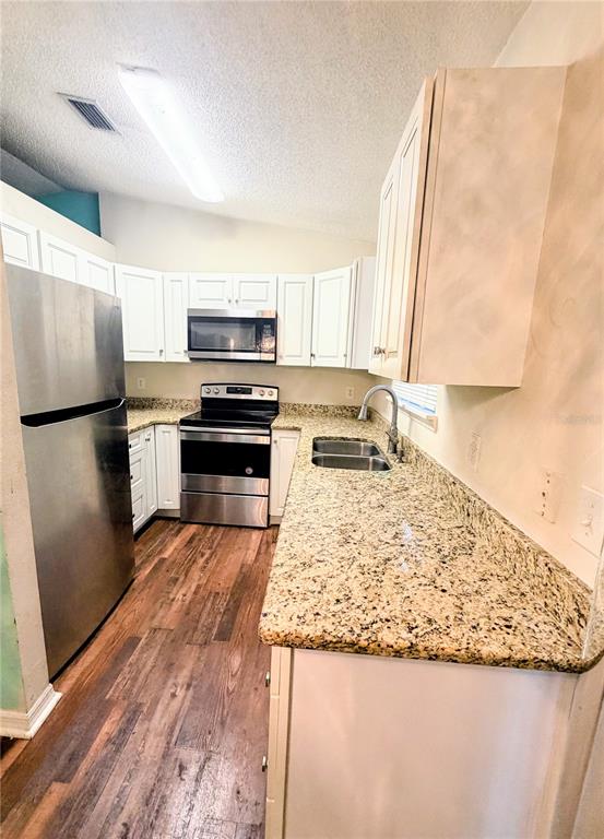 A kitchen features white cabinets, granite countertops, stainless steel appliances, and wood-look flooring — 2404 NE 32ND PLACE, OCALA, FL