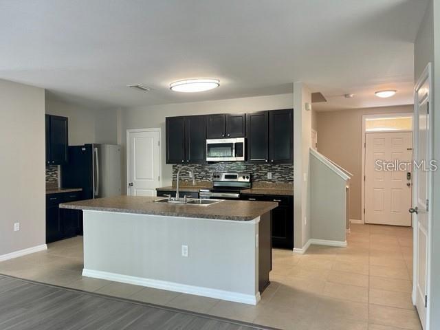 A kitchen features dark cabinets, a central island with a sink, and light tile flooring — 833 WILTONWAY DRIVE, PLANT CITY, FL