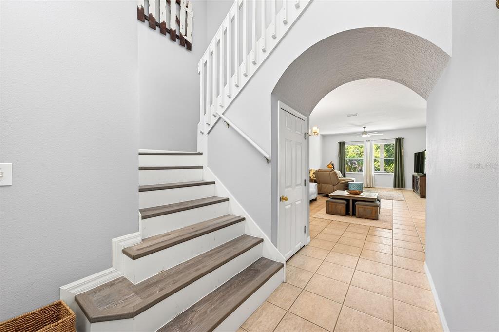 A staircase with wood-look treads leads to an arched entryway opening into a living room — 14933 YORKSHIRE RUN DRIVE, ORLANDO, FL