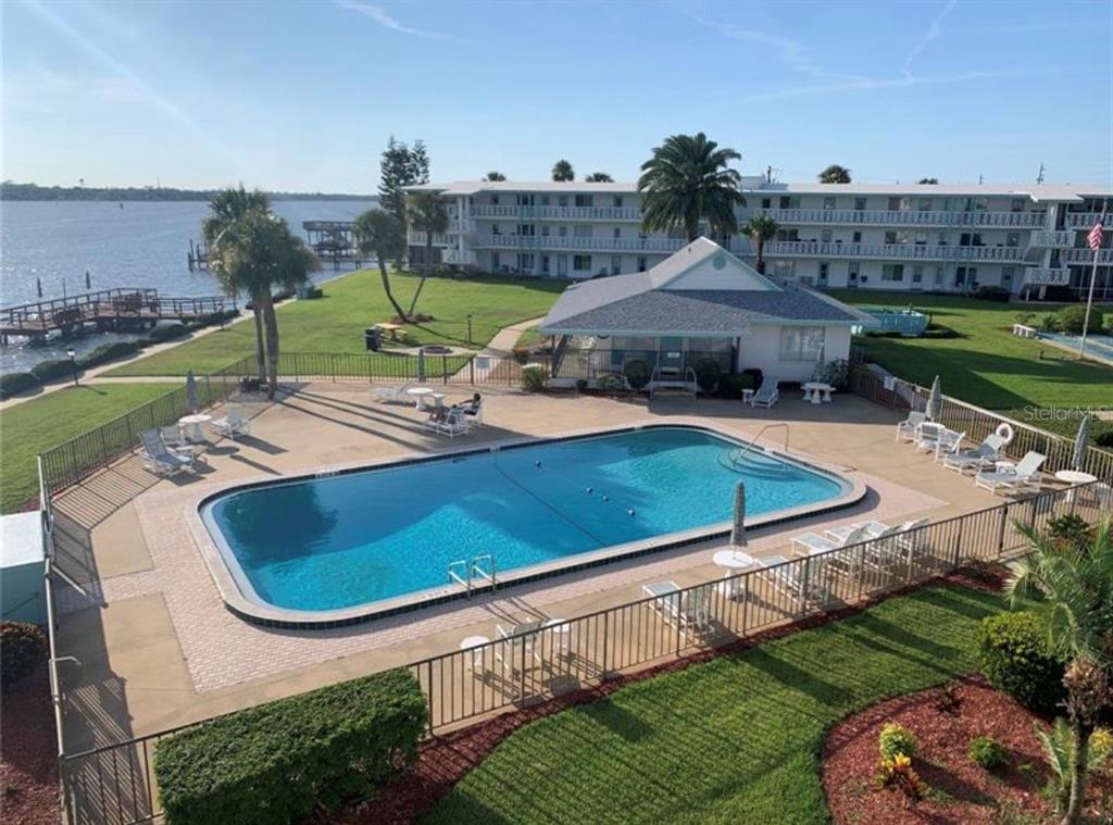 An elevated view of a rectangular swimming pool with lounge chairs and a waterfront building — 3009 N HALIFAX AVENUE UNIT 2, DAYTONA BEACH, FL