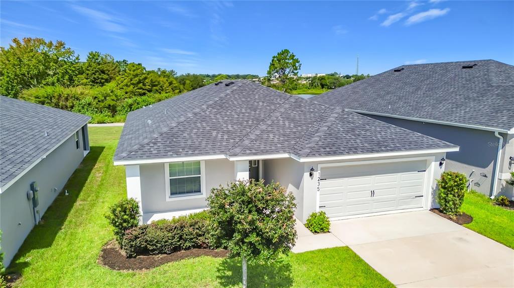 A single-story house with a gray shingled roof, white garage door, and green front lawn — 1235 MOUNTAIN FLOWER LANE, DAVENPORT, FL