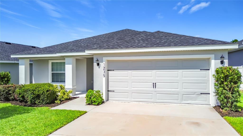 A single-story house with a gray garage, dark front door, and a manicured front lawn — 1235 MOUNTAIN FLOWER LANE, DAVENPORT, FL