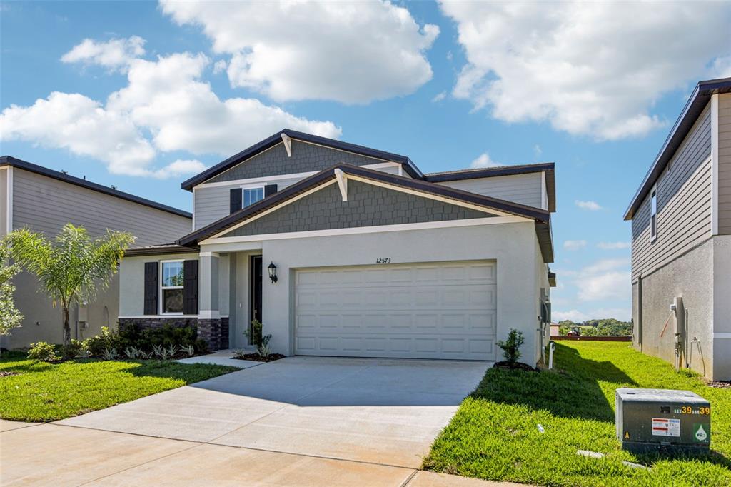 A two-story suburban house with a gray stucco facade, shingled gables, and a concrete driveway — 12573 HOMELAND DRIVE, DADE CITY, FL