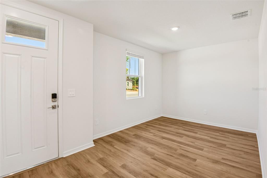 A bright room with white walls, wood-look flooring, a single window, and a front door — 12573 HOMELAND DRIVE, DADE CITY, FL