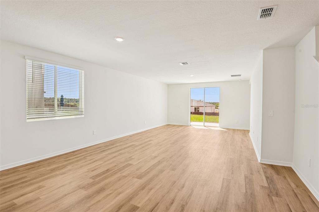 An empty room features light wood-look flooring, white walls, a window, and sliding glass doors — 12573 HOMELAND DRIVE, DADE CITY, FL