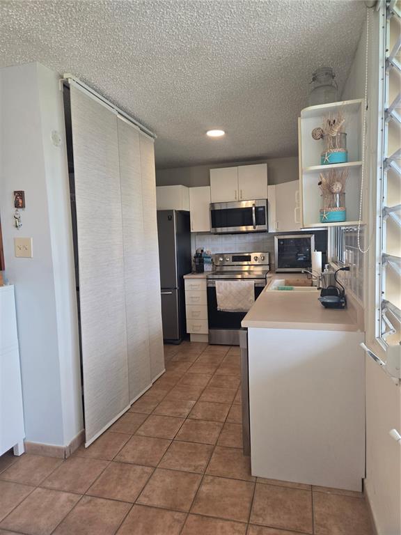 A galley kitchen features white cabinets, stainless steel appliances, and tan tile flooring — 368 CAMINO LAS PICUAS UNIT 3209, RIO GRANDE, PR