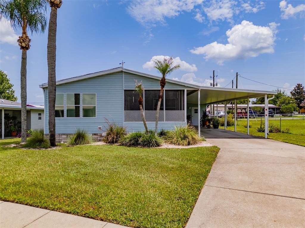 A light blue manufactured home features a screened-in porch, a carport, and a grassy lawn — 37716 NEWPORT DRIVE, ZEPHYRHILLS, FL