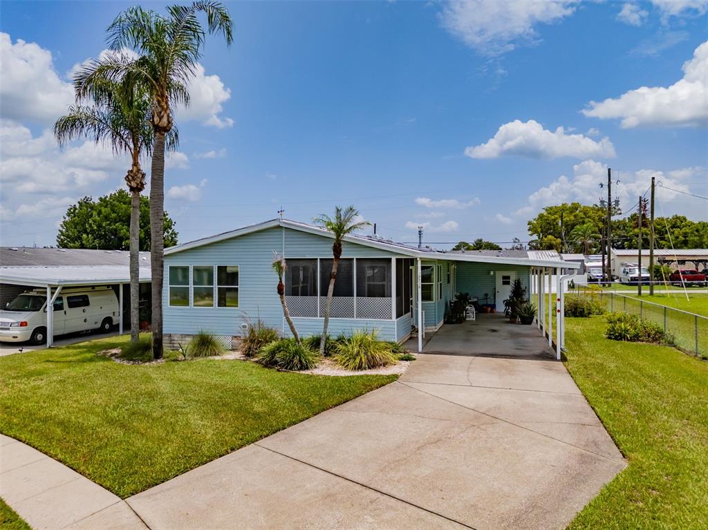 A light blue manufactured home features a screened-in porch, a carport, and a palm tree — 37716 NEWPORT DRIVE, ZEPHYRHILLS, FL