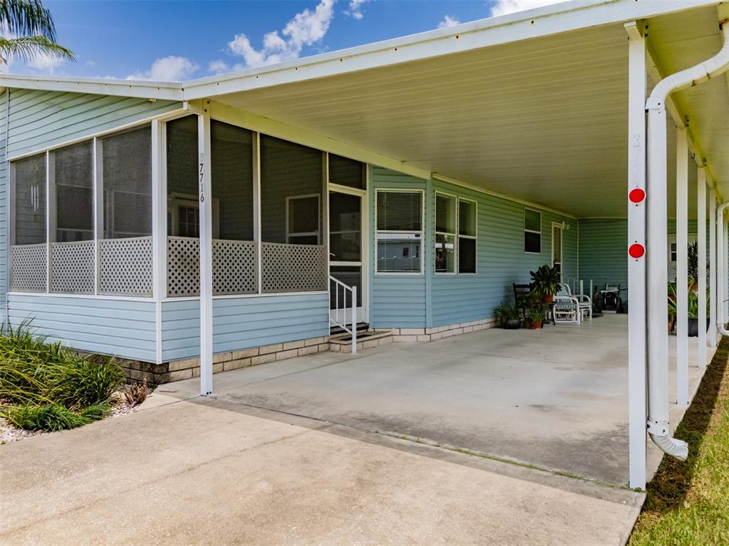 A light blue mobile home features a screened-in porch and a large attached carport — 37716 NEWPORT DRIVE, ZEPHYRHILLS, FL