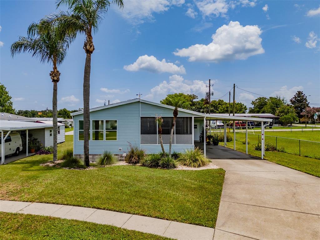 A light blue manufactured home features a screened front porch and an attached carport — 37716 NEWPORT DRIVE, ZEPHYRHILLS, FL